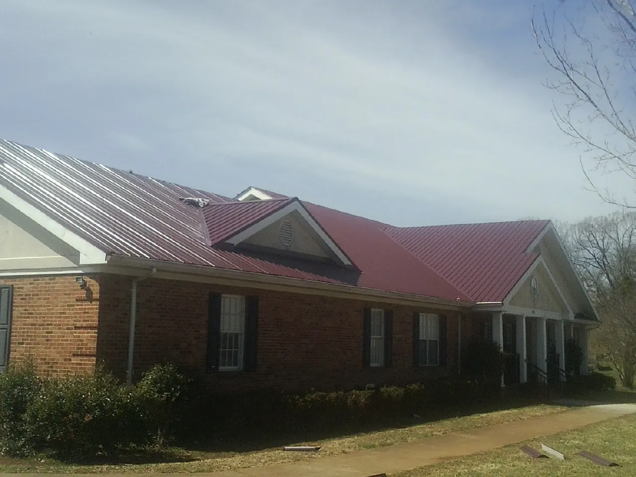 Red metal roof with gabled entries on a long brick building, from a Hail Damage Roof Repair job in Glasford
