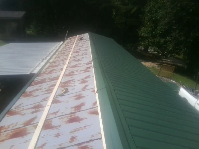 Old rusted panels beside newly installed green metal roofing — Wind Damage Roof Repair by Roofing Brothers in Glasford