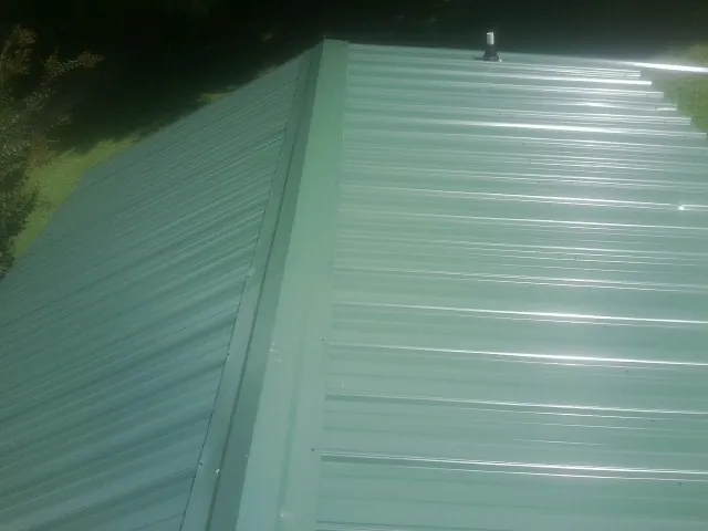New green metal panels meeting at the ridge of a roof — Flat Roof Repair work by our crew in Glasford