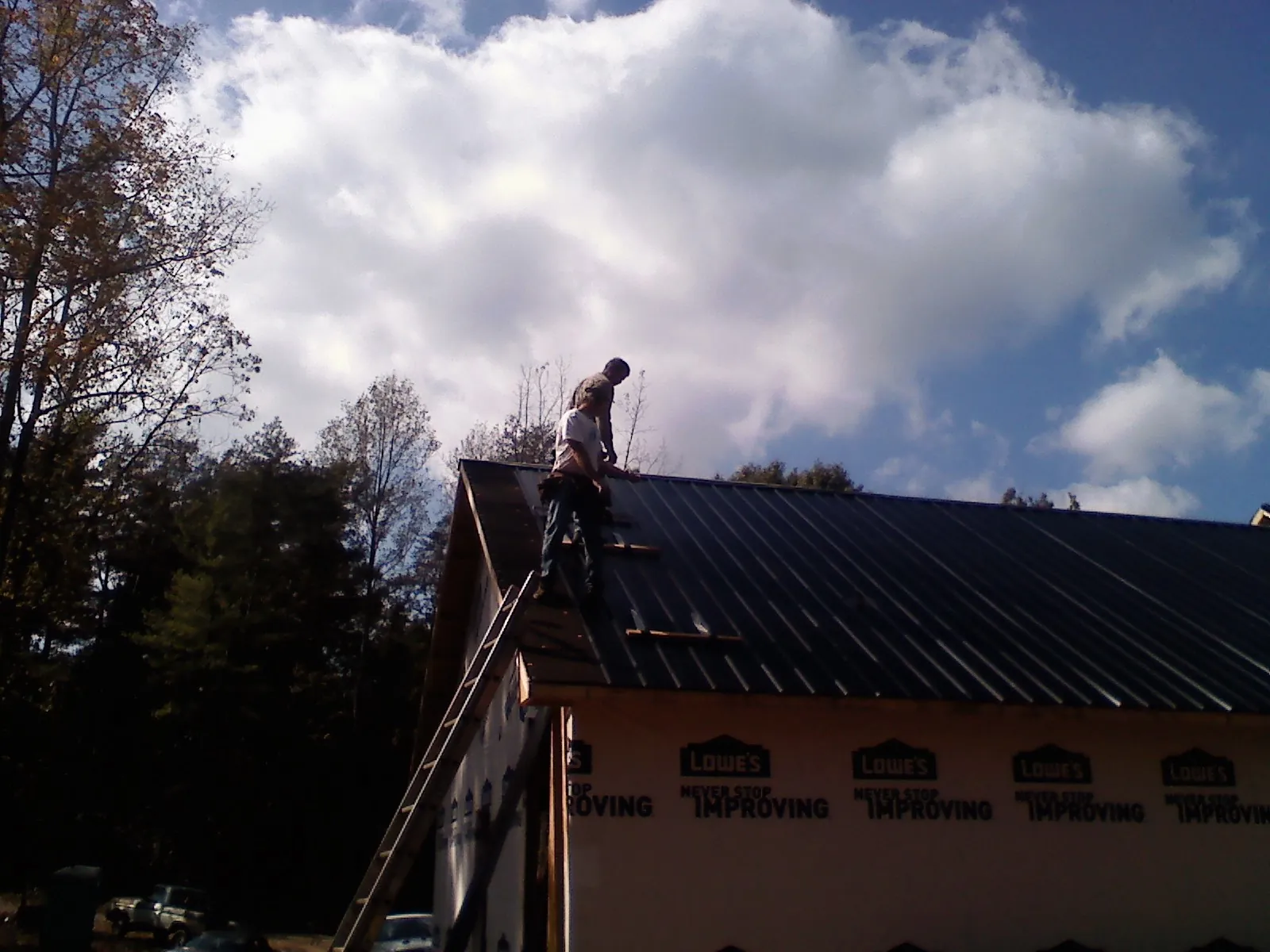 Roofer fastening dark metal panels high against a cloudy sky, from a Roof Inspection job in Glasford