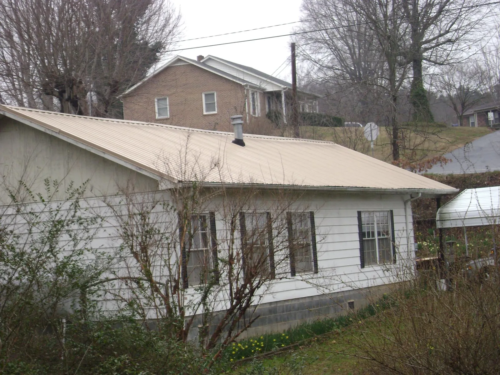Tan metal roof on a white sided house set into a hillside — Commercial Roofing by Roofing Brothers in Glasford